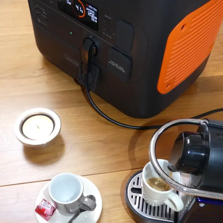 Das Foto zeigt eine Nespresso-Maschine, die an eine Powerstation Jackery Explorer 2000 Pro angeschlossen ist. Der Kaffee läuft in eine Tasse, das Display der Powerstation zeigt einen aktuellen Verbrauch von ca. 1200 Watt.