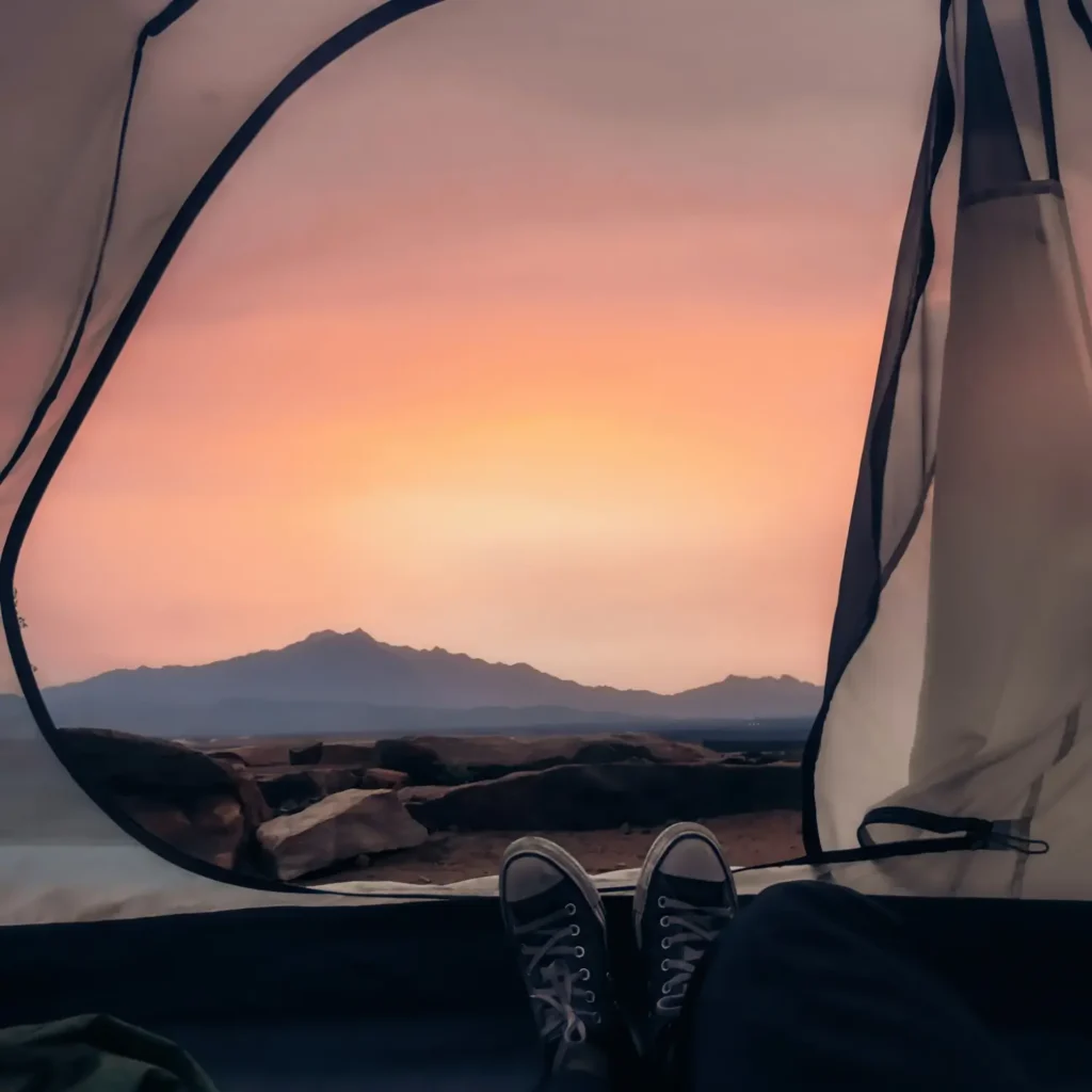 Das Foto zeigt den Blick aus einer geöffneten Zeltöffnung auf eine Berglandschaft bei Sonnenuntergang im Hintergrund.